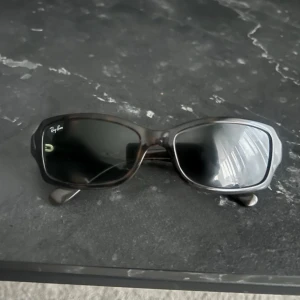  Solglasögon från Ray-Ban - Ray-Ban RB2130 Rituals Pande med mörka glas och rektangulja bågar. Unisex-modell som sitter bra och har Ray-Ban-logga på ena glaset.  Pris kan diskuteras 