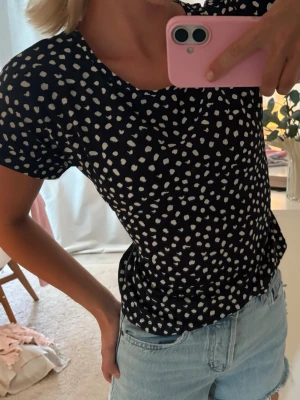 Svart prickig topp med kort ärm - Snygg marinblå topp med vita prickar och rund halsringning. Kortärmad modell som passar perfekt till jeans eller kjol. Enkel men trendig design som ger en cool vibe till din outfit.