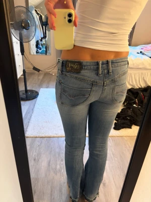 Ljusblå bootcut jeans från Replay - Säljer dessa lågmidjade vintage jeans med skitsnygga lila mönster och snygga detaljer nere vid foten🥰På byxorna står det att storleken är 29 men jag skulle säga att de är som storlek 25/26!