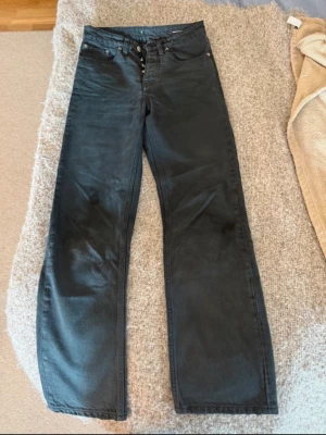 Svarta raka jeans med hög midja - Säljer ett par svarta jeans med rak passform och hög midja. Jeansen har klassisk femficksdesign och knappgylf. Materialet är kraftigt denim som ger en snygg och tidlös look. Perfekta till en avslappnad stil.