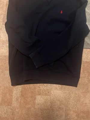 Mörkblå hoodie från Polo Ralph Lauren - Snygg mörkblå hoodie från Polo Ralph Lauren med den klassiska röda loggan broderad på bröstet. Hoodien har en avslappnad passform, långa ärmar och ribbade muddar. Perfekt för en casual och stilren look. Köpte den på zalando
