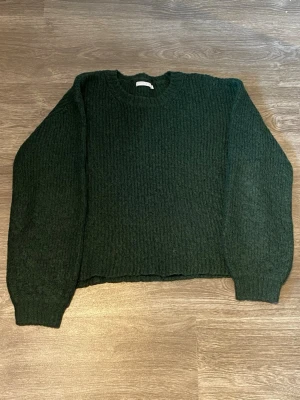 Mörkgrön stickad tröja - Mörkgrön stickad tröja med rund halsringning och långa ärmar. Tröjan har ett stickat och skönt material och ribbstickade muddar vid ärmslut och nederkant. 