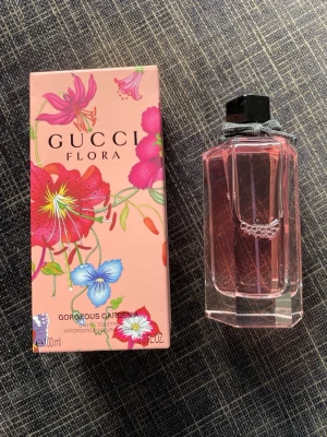 Gucci Flora Gorgeous Gardenia parfym - Gucci Flora Gorgeous Gardenia är en parfym med blommig doft i en elegant, sexkantig glasflaska med rosa vätska och svart kork. Förpackningen är dekorerad med färgglada blommor i rosa, rött, blått och grönt på en ljusrosa bakgrund. Volym: 100 ml.