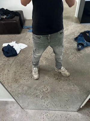 Supply and demand jeans  - Säljer ett par grå slim fit jeans med coola vita färgstänk och slitningar. Jeansen har klassisk femficksmodell och smal passform som sitter snyggt längs benen. Perfekta för dig som vill ha en trendig och avslappnad look.