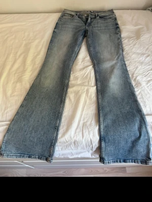 Ljusblå bootcut jeans - Säljer ett par ljusblå bootcut jeans med klassisk femficksmodell och dragkedja. Jeansen har en snygg tvättad look och breda ben som ger en retrovibe. Perfekta för dig som gillar avslappnad stil och vill ha ett par jeans som sticker ut.
