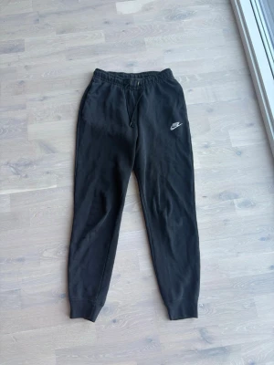 Svarta mjukisbyxor från Nike XS - Svarta mjukisbyxor från Nike med dragsko i midjan och resår vid bensluten. Klassisk Nike-logga på vänster ben. Tillverkade i mjukt och bekvämt material som passar perfekt för chill eller träning.