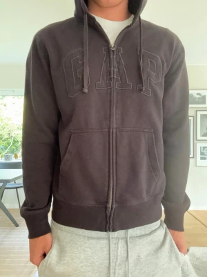 Svart ziphoodie från GAP - Storek M men skulle säga att den sitter mer åt S hållet! Säljer en svart hoodie från GAP med dragkedja framtill och stor broderad GAP-logga på bröstet. Hoodien har huva med dragsko och två stora fickor framtill. Perfekt för chill dagar och enkel att matcha med allt.