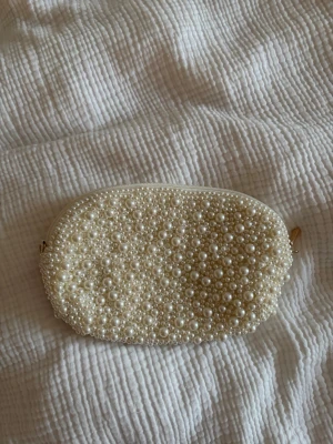 Vit kuvertväska med pärlor och kedja - Säljer en superfin vit kuvertväska täckt med pärlor i olika storlekar. Väskan har en tunn guldfärgad kedja som axelrem som man kan ta av och på ⭐️