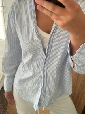 Blårandig perfekt skjorta från Zara - Säljer en blårandig skjorta från Zara i storlek XS. Skjortan har klassisk krage, knappar framtill och långa ärmar. Tillverkad i tunn bomull som känns luftig och skön. Perfekt nu inför jobb och skola!