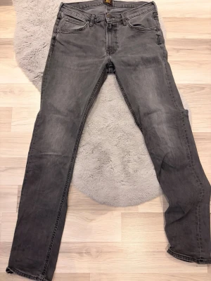 Gråa slim fit jeans från Lee - Snygga gråa slim fit jeans med klassisk femficksdesign och normal midja. Jeansen har en lätt tvättad look och raka ben. Perfekta för dig som gillar en stilren och enkel vardagsstil.