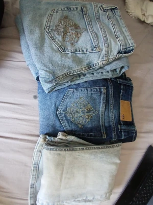 Tre stycken jeans - Säljer ett par blå jeans från 157 med snyggt guldbroderi på bakfickan. Klassisk femficksmodell i denim med normal passform och raka ben. Perfekta för dig som gillar detaljer och vill ha ett par jeans som sticker ut lite extra.