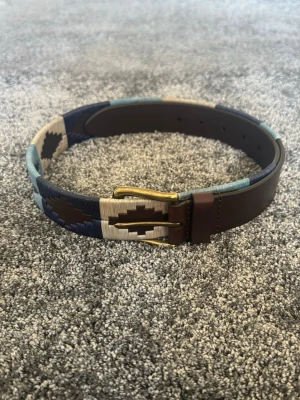 Brunt och blått mönstrat skärp - Snyggt skärp i brunt skinn med detaljer i blått, beige och mörkblått. Skärpet har ett coolt geometriskt mönster och metallspänne i mässing. Perfekt accessoar för att lyfta din outfit.