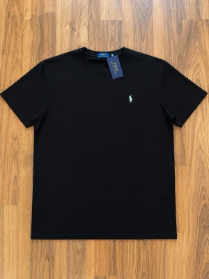 Svart t-shirt från Polo Ralph Lauren large - Svart t-shirt från Polo Ralph Lauren med klassisk rund hals och liten broderad logga på bröstet. Tillverkad i mjuk bomull och har en enkel, stilren design som passar till det mesta.