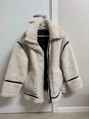 Beige teddyjacka med svarta detaljer - Jackan är endast använd en gång.