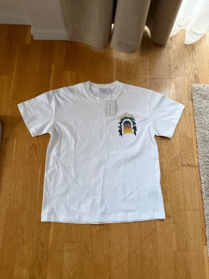 Vit Casablanca t-shirt  - Vit t-shirt från Casablanca med färgglatt tryck på bröstet och stort grafiskt motiv på ryggen med texten 'Avenida Casablanca'. Klassisk passform och rund hals. Perfekt för dig som gillar streetwear och snygga prints.