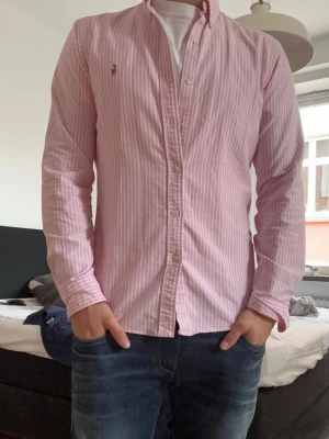 Rosa och vit randig Ralph lauren  skjorta - Säljer en rosa och vit randig Ralph Lauren skjorta. Den är as snygg och är perfekt om man vill stå ut. Perfekt för dig som gillar en clean och fräsch stil.                                                                        Kom pm för frågor!