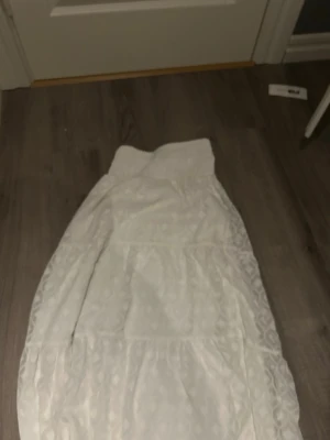 Vit långkjol från Gina Tricot - Säljer en vit långkjol från Gina Tricot med bred resår i midjan. Kjolen har ett diskret blommigt mönster och är tillverkad i ett lätt och luftigt material, perfekt för varmare dagar.