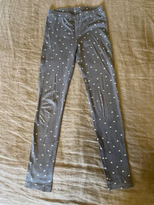 Mörkgråa leggings med silvriga hjärtan - Supersöta mörkgrå leggings med små vita hjärtan över hela tyget. Stl.122/128 från Cubus 