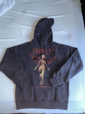 Svart Nirvana In Utero hoodie - Säljer en svart hoodie med Nirvana In Utero-tryck på framsidan. Hoodien har huva med dragsko och ribbade muddar vid ärmar och nederkant. Materialet känns mjukt och bekvämt, perfekt för dig som gillar bandmerch och vill ha en avslappnad stil.