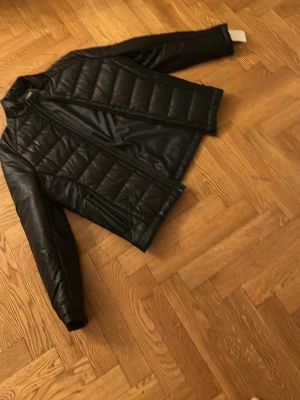 Svart pufferjacka med dragkedja - Snygg svart pufferjacka med quiltad design och raka ärmar. Jackan har en hög krage och stängs med dragkedja framtill. Perfekt för kalla vinterdagar och ger en stilren look.
