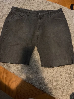 Mörkgrå jeansshorts - Säljer ett par mörkgrå jeansshorts från Mc Gordon. Midja 44. Avklippta från ett par jeans. Använda men i fint skick. Säljer för att dom är alldeles för stora och inte används 