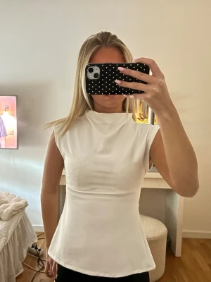 Vit ärmlös topp med hög krage - Säljer en stilren vit topp med hög krage, öppen i ryggen. Använd fåtal gånger