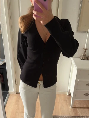 Svart v-ringad långärmad topp - Säljer en svart långärmad tröjamed v-ringning  framtill. Snygg och enkel modell som passar till mycket. Figurnära passform och mjukt material. 