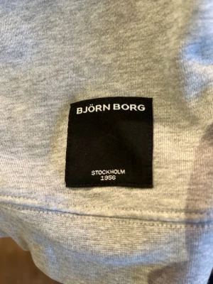 Grå sweatshirt från Björn Borg - Säljer en stilren grå sweatshirt från Björn Borg med rund halsringning och diskret svart patch med logga framtill. Tröjan är i mjukt material och har klassisk passform, perfekt för en avslappnad look.