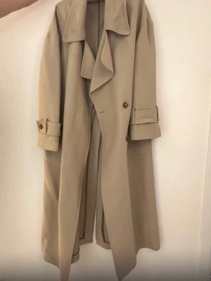 Beige klassisk trenchcoat med bälte - Beige, ofodrad kappa från Gant i trenchcoatmodell.   54% polyamid, 46% viskos