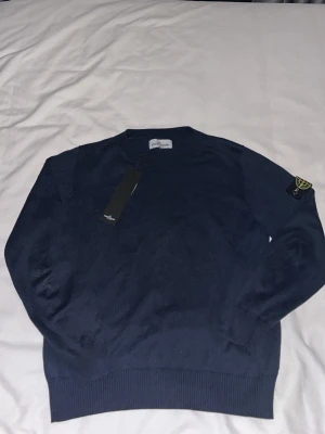 Mörkblå stickad tröja Stone Island - Snygg mörkblå stickad tröja från Stone Island med klassisk patch på vänster ärm. Tröjan har rund halsringning, ribbade muddar och är tillverkad i mjukt material som passar perfekt till höst och vinter,hör bara av er om någon funderingar i dm🤞🏼☺️