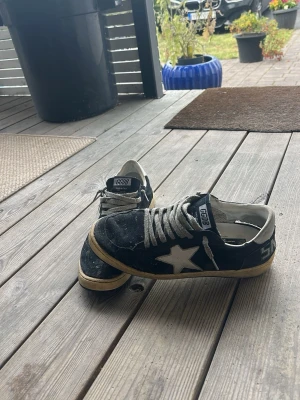 Mörkblå Golden goose sneakers - Snygga svarta sneakers från GGDB med vit stjärndetalj på sidan och vita skosnören. Skorna har en låg profil och beige sula med vintagekänsla. Ovandelen är i mocka och insidan är vit. Gått sönder i baken därför lågt pris. Skriv vid funderingar/frågor 