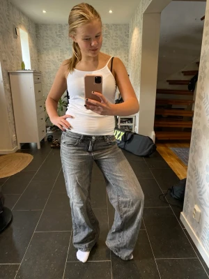 Baggy grå jeans med låg midja - Säljer ett par grå baggy jeans med låg midja och raka, vida ben. Jeansen har klassiska fem fickor och ljusa slitningar för en cool vintagekänsla. Perfekta för dig som gillar avslappnad och trendig stil. Obs - de är lite slitna längst ner pga att de varit lite för långa för mig. 