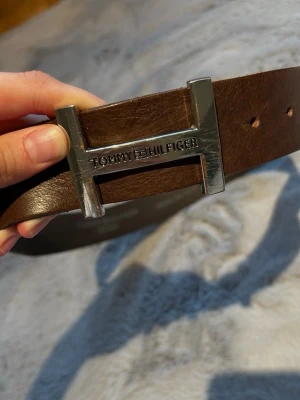 Skärp - Brunt skärp från Tommy Hilfiger. Säljs då den inte används. Storlek: 90 cm. Inga större defekter, endast lite märken på spännet, se sista bilden. Skriv för fler bilder 💕