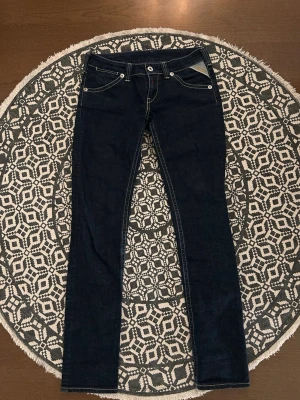 Mörkblå raka jeans från Replay - Snygga mörkblå jeans från Replay med raka ben och kontrastsömmar. Klassisk femficksmodell med silverfärgade nitar och läderpatch bak i midjan. Jeansen har låg midja och är tillverkade i ett mjukt denimtyg som sitter skönt.