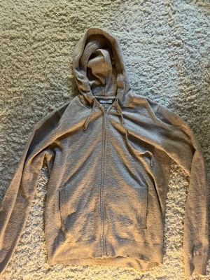 Beige  zip-hoodie med fickor - En stilren beige  hoodie med dragkedja framtill, två stora fickor och justerbar huva med snören. Tillverkad i mjukt stickat material som passar perfekt för en avslappnad look. Långärmad och enkel att matcha med det mesta.