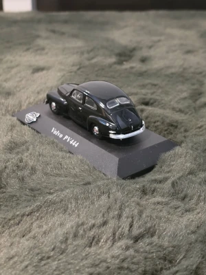 Modellbil Volvo PV444 svart - Säljer en detaljerad modellbil av Volvo PV444 i svart färg. Bilen är tillverkad i metall och plast och står på en svart bas med modellnamnet tryckt på. Perfekt för samlare eller som dekoration.