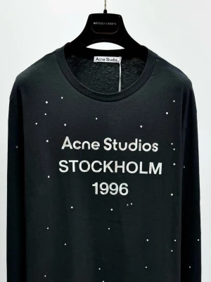 Svart långärmad topp Acne Studios - Svart långärmad topp från Acne Studios med tryck 'STOCKHOLM 1996' framtill. Toppen har små vita prickar över hela plagget som ger en cool touch. Rund halsringning och mjukt material som känns skönt mot huden.