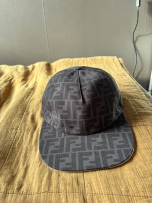 Svart Fendi keps  - Säljer en svart keps med stilrent monogrammönster över hela kepsen. Klassisk form med böjd skärm och justerbar baksida. Materialet känns slitstarkt och passar perfekt till streetwear eller en clean look. Skriv till mig för frågor!