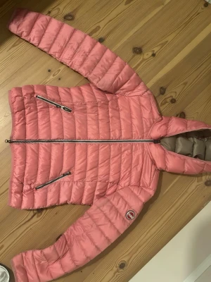Rosa dunjacka från Colmar - Snygg rosa dunjacka från Colmar med huva och två dragkedjeförsedda fickor framtill. Jackan har quiltad design och en rund Colmar-logga på ärmen. Perfekt för kalla vinterdagar och riktigt lätt att bära.