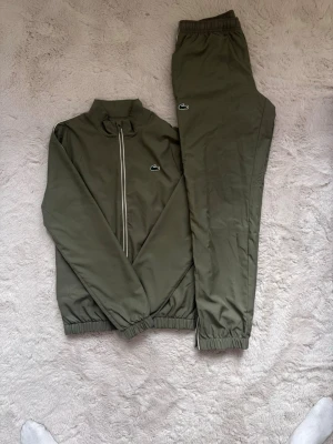 Dress från Lacoste - Säljer en olivgrön dress från Lacoste med matchande jacka och byxor. Perfekt för sport eller chill. Pris kan diskuteras.