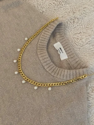 Guldfärgat halsband med pärlor - Snyggt halsband i guldfärgad rostfritt med kedjedesign och vita pärlor som hänger längs hela kedjan. Perfekt för att ge din outfit en trendig och elegant touch. Passar till många olika stilar och är lätt att matcha med andra accessoarer.