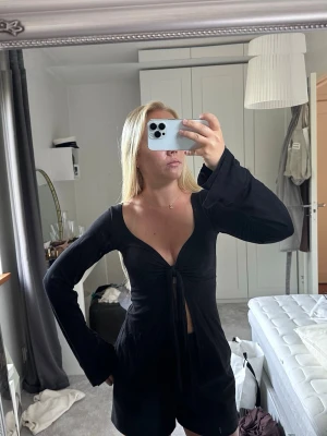 Svart långärmad topp med snörning - Snygg svart topp med djup v-ringning och långa ärmar. Toppen har snörning framtill som ger en cool detalj och croppad passform. Perfekt för dig som vill ha en trendig och stilren look.