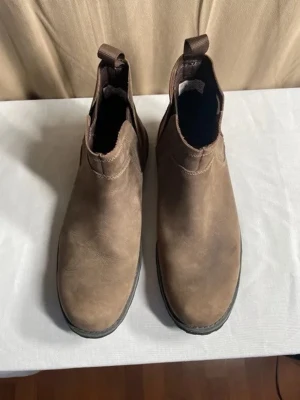 Bruna Chelsea boots från Timberland - Säljer ett par bruna Chelsea boots från Timberland i storlek 44.5. Skorna är i mockaliknande material med elastiska paneler på sidorna och dragflikar både fram och bak. Klassisk rund tå och robust sula för en stilren look. I mycket fint skick.