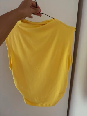 Gul ärmlös linnetopp - Snygg gul linnetopp i mjukt material. Toppen är ärmlös och har en enkel, clean design som passar perfekt till jeans eller kjol. Perfekt för varma dagar och enkel att styla med accessoarer.