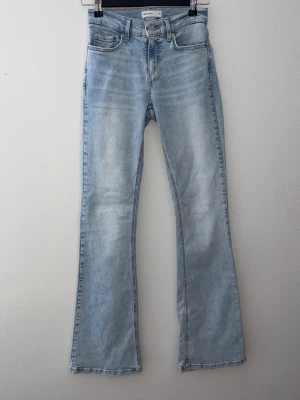 Ljusblå low waist bootcut jeans - Säljer ett par ljusblå low waist bootcut jeans med klassisk femficksdesign och hög midja. Jeansen har en snygg tvättad look och är tillverkade i denim med lätt stretch. Perfekta för dig som gillar en avslappnad men trendig stil.