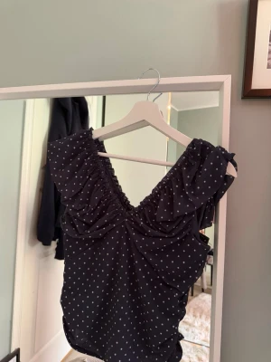 Svart prickig volangtopp - Snygg svart topp med vita prickar och volangdetaljer vid axlarna. Nästan helt oanvänd💕