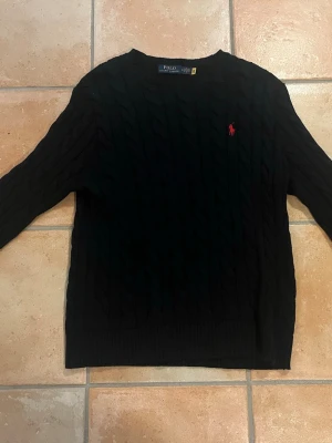 Mörkblå kabelstickad tröja Polo Ralph Lauren - Kabelstickad mörkblå från Polo Ralph Lauren med klassisk röd logga broderad på bröstet. Den kostar originellt 2600 kronor på Ralph Lauren hemsidan men jag säljer den för 1000kr men priser kan förhandlas! 