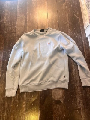 Ljusblå sweatshirt från Dickies - Snygg ljusblå sweatshirt från Dickies med klassisk rund halsringning och liten logotyp på bröstet. Tröjan har ribbade muddar vid ärmslut och nederkant. Perfekt för en avslappnad och stilren look. Skriv om ni har frågor!