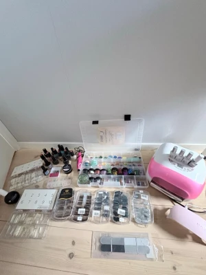 Stort kit med nagel saker - Säljer ett komplett nagelkit med flera nagellack i olika färger som svart, guld, blått, grönt och nude. Inkluderar glitter, nageldekorationer, tippar, filar, UV-lampa och verktyg för nagelförlängning, gelé, topp cote och massa mer. Gelén är halv fylld och de mesta är använt. Men det finns massor kvar.Perfekt för dig som vill fixa snygga naglar hemma och experimentera med olika stilar.