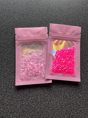 Rosa och neonrosa nagelstenar - Två påsar med små dekorationsstenar för naglar i rosa och neonrosa nyanser. Stenarna är runda och har en glittrande yta som ger extra effekt till nageldesignen. Perfekt för att skapa kreativa och personliga naglar.